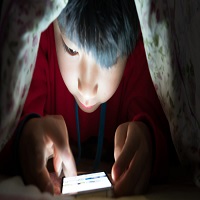 Jeune garçon sous une couverture, tenant un smartphone