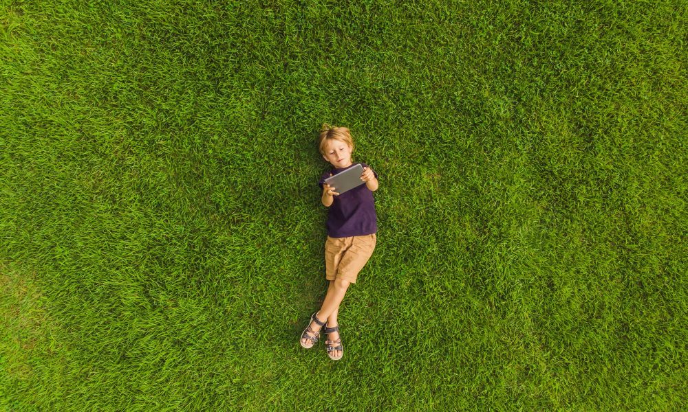 Jeune garçon allongé sur l’herbe et regardant une tablette