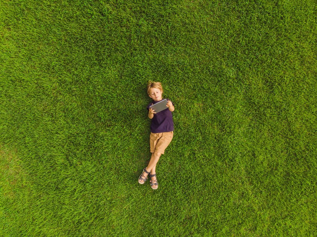 Jeune garçon allongé sur l’herbe et regardant une tablette