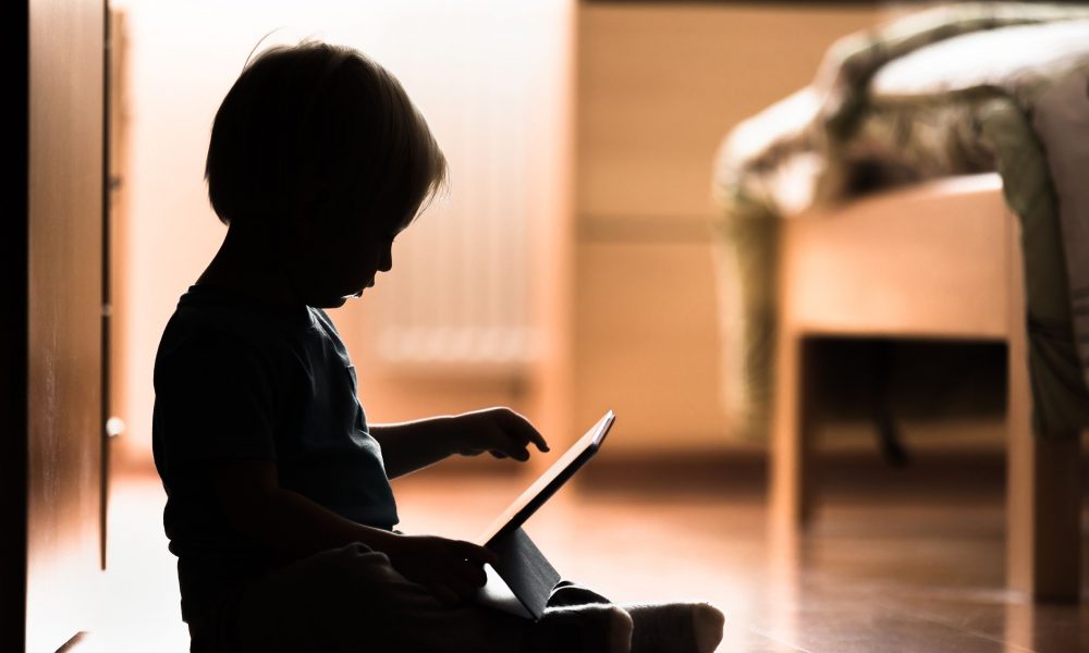 Silhouette d’un enfant assis sur le plancher regardant une tablette