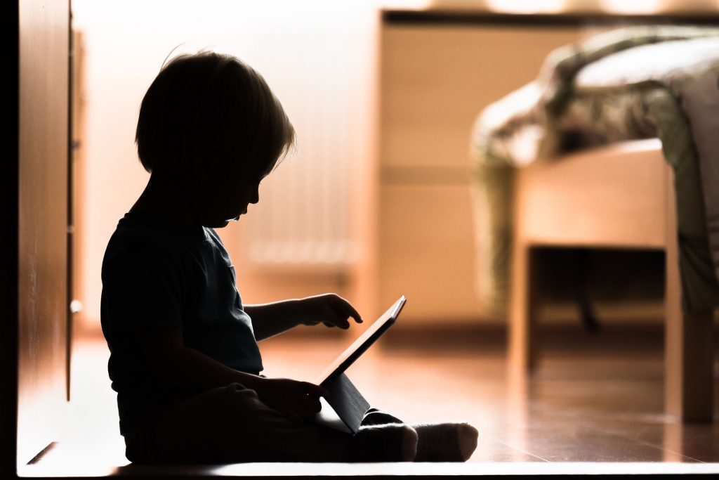 Silhouette d’un enfant assis sur le plancher regardant une tablette