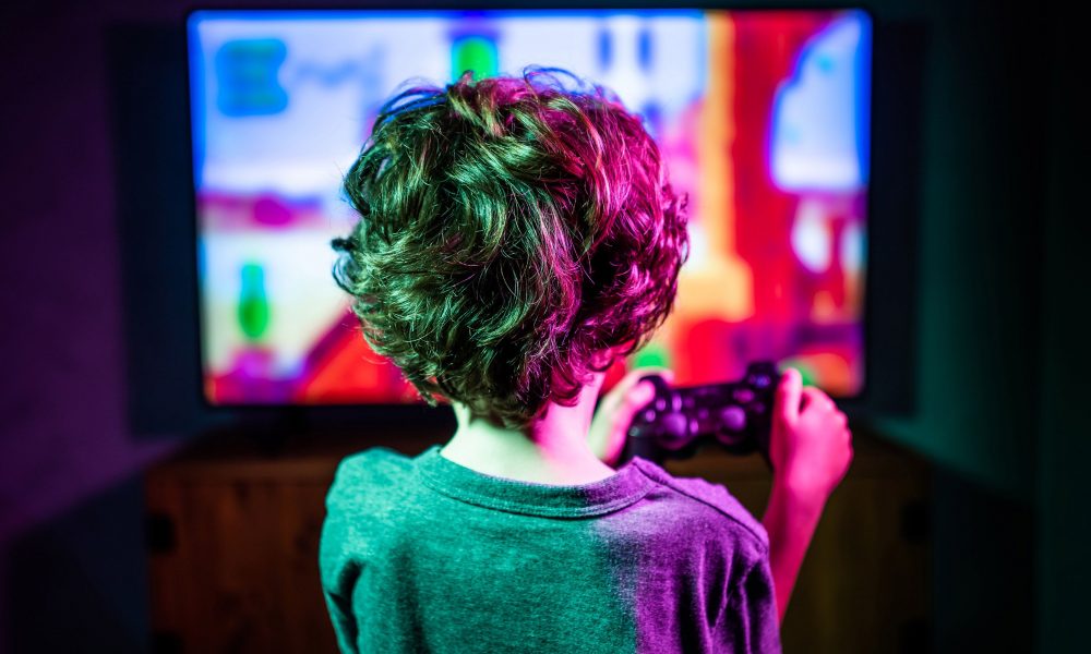 Un enfant qui tient une manette de jeu à la main et qui est posté devant un large écran TV.