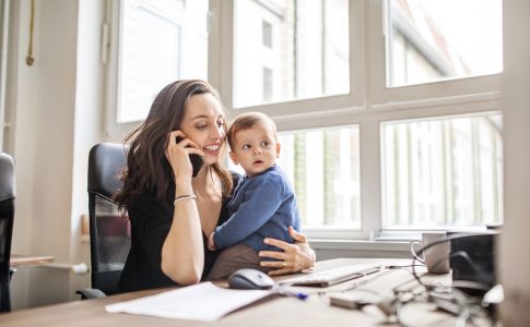 Une mère tenant son enfant tout en étant pendue à son téléphone et scotchée à son bureau de travail.