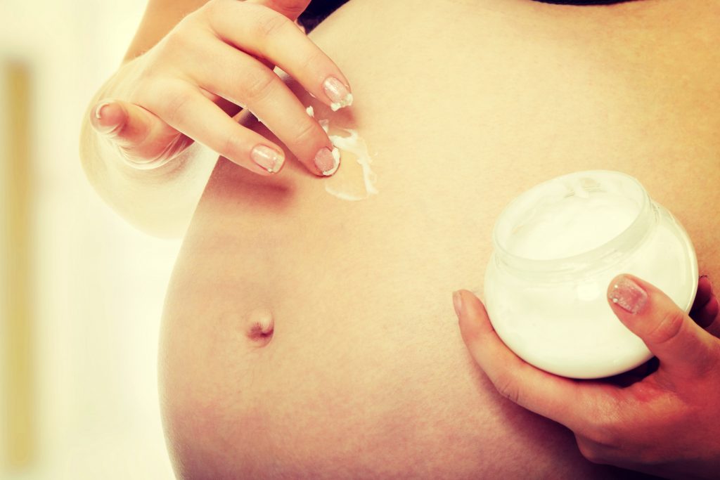 Une femme enceinte en train d’appliquer une crème cosmétique sur son ventre.