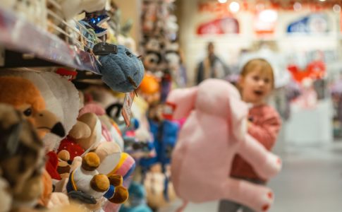 Une petite fille dans un magasin tenant un éléphant rose, une couleur stéréotypée comme dans les publicités pour jouets.
