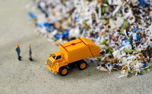 L’image représentative d’une décharge de déchets plastiques avec un mini camion poubelle et des personnages discutant recyclage jouets.