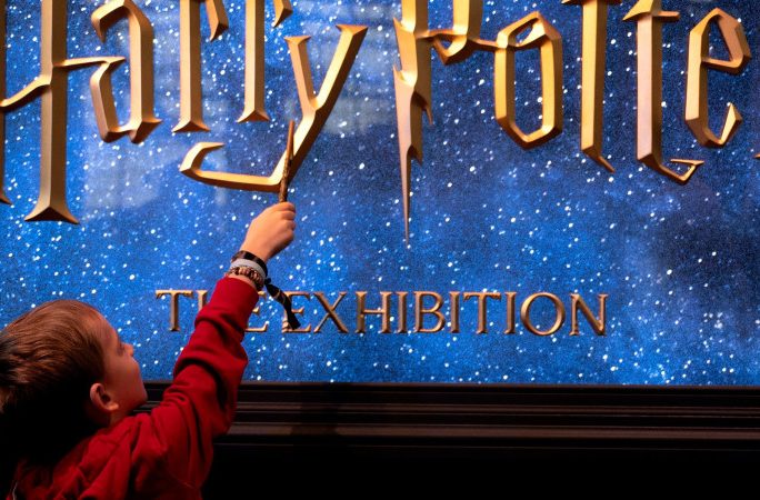 Un petit garçon avec sa baguette magique devant l’affiche de l’exposition Harry Potter