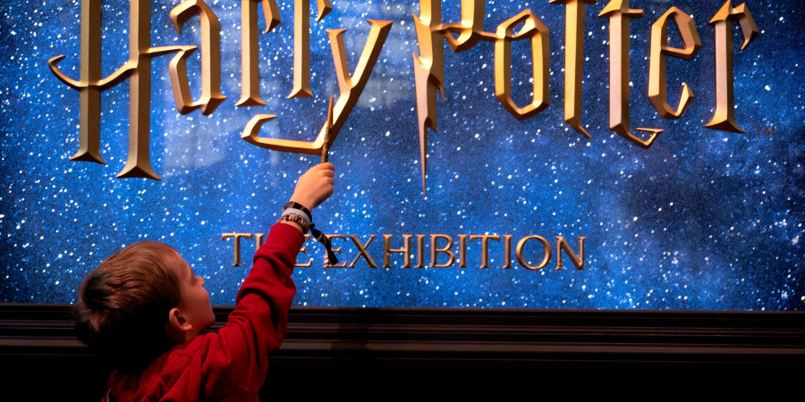 Un petit garçon avec sa baguette magique devant l’affiche de l’exposition Harry Potter