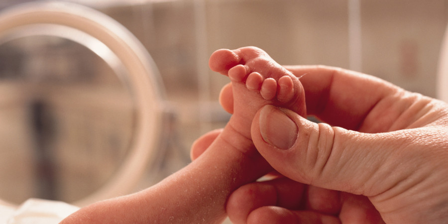 Un nouveau-né dans une couveuse avec le pied en l’air, tenu par une main d’adulte.