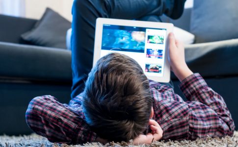 Un utilisateur mineur allongé sur le tapis d’un salon, en train de visionner des contenus vidéo en ligne.