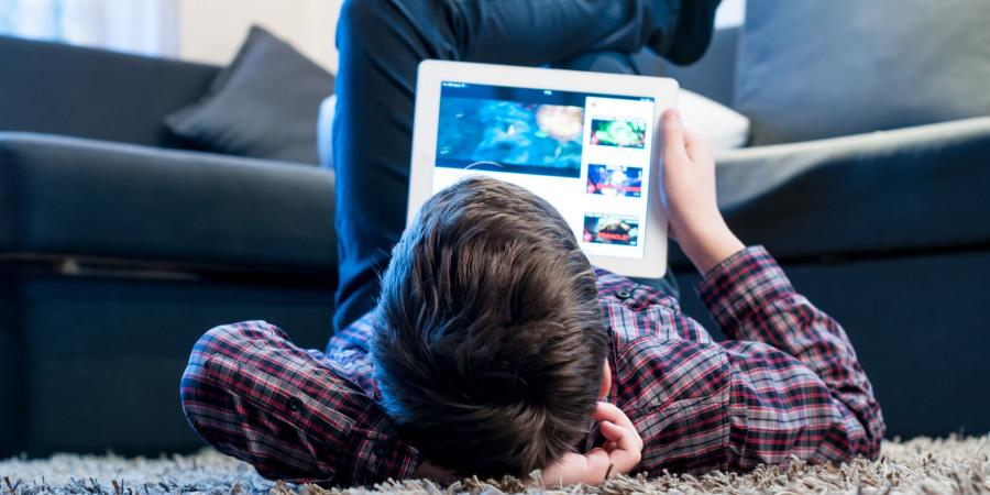 Un utilisateur mineur allongé sur le tapis d’un salon, en train de visionner des contenus vidéo en ligne.