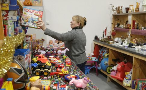 Une des gérantes du supermarché inversé et magasin gratuit en Corse en train de ranger une boîte de Monopoly sur une étagère plein de jouets.