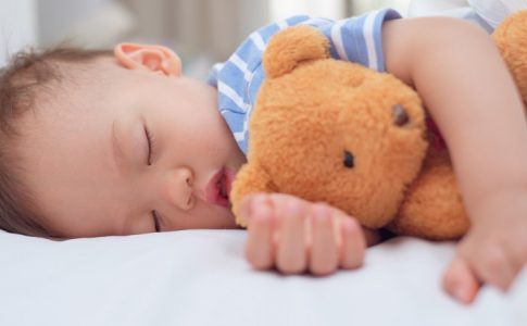 Un bébé profondément endormi avec son ours doudou, une représentation claire du réconfort apporté par les peluches.