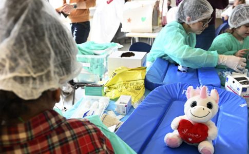 Une peluche licorne assise sur une table à l’hôpital des nounours, entourée de jeunes enfants en pleine découverte médicale