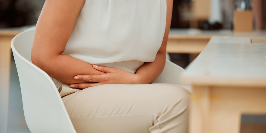 Une femme assise à son bureau se tient le bas du ventre afin d’apaiser ses règles douloureuses.