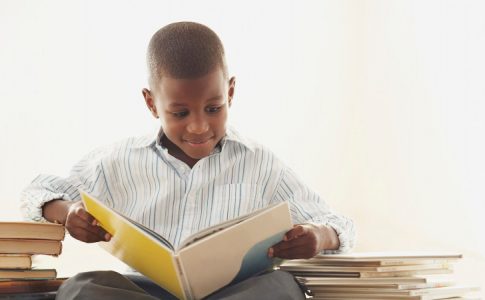 Un jeune garçon lisant des livres, un moyen d’améliorer ses notes à l’école tout comme les contenus audios.
