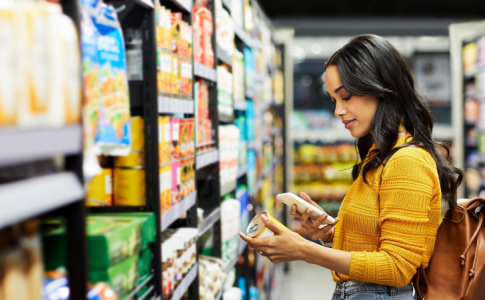Dans un supermarché, une mère de famille en train de comparer le prix des aliments sains sur son mobile.
