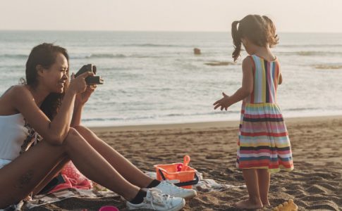 Une maman à la plage en train de prendre des clichés de sa fille avec un polaroid, rejetant le partage photo enfants sur réseaux sociaux.