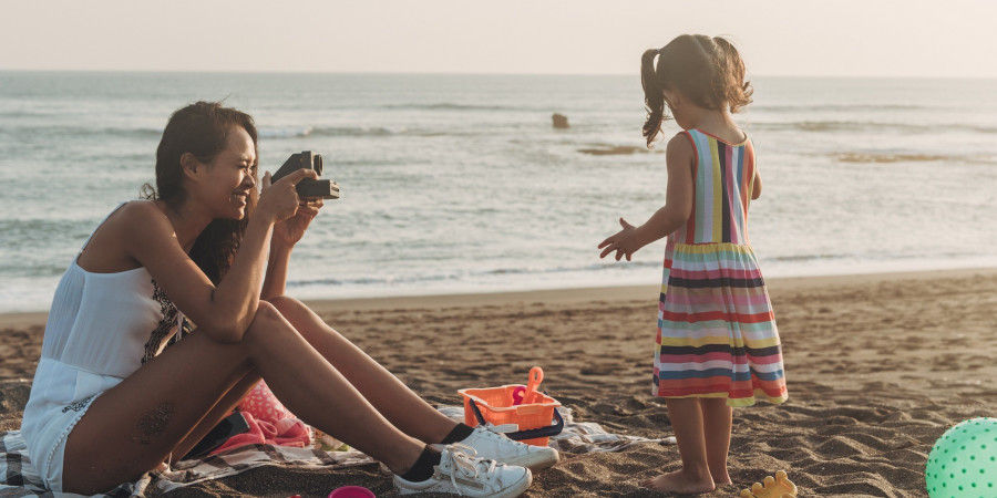 Une maman à la plage en train de prendre des clichés de sa fille avec un polaroid, rejetant le partage photo enfants sur réseaux sociaux.
