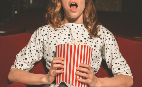 Une femme ébahie en train de regarder un film au cinéma, une illustration du phénomène de « popcorn brain ».