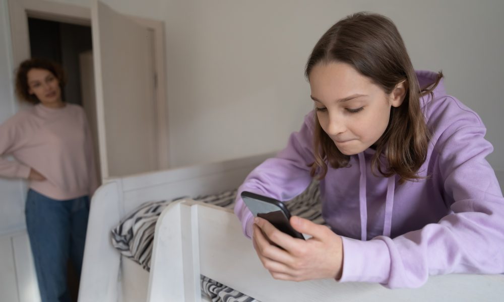 Effets negatifs ecrans : Une adolescente en train de regarder dans son smartphone et observee par sa mere
