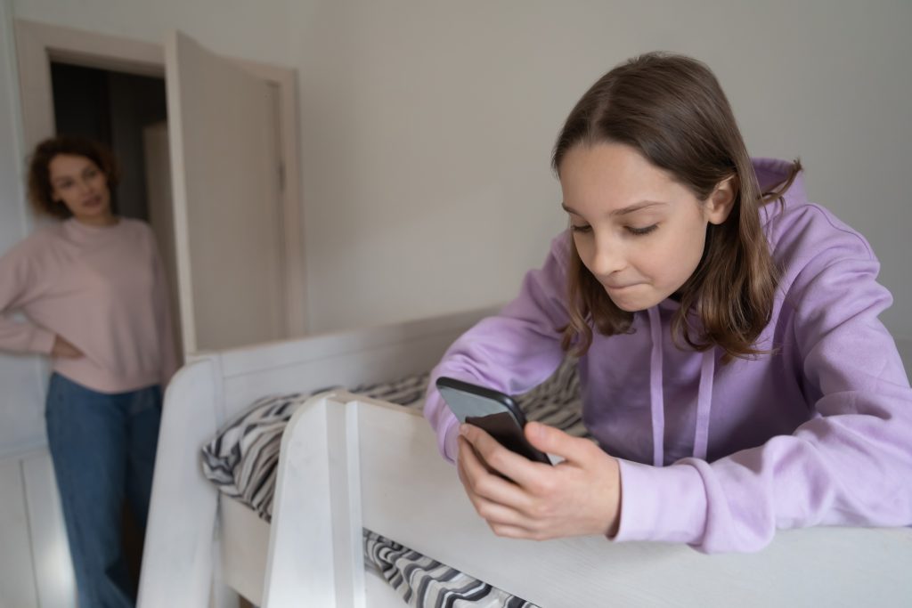 Une adolescente en train de regarder dans son smartphone et observee par sa mere