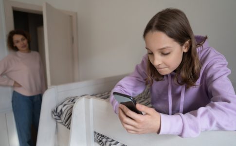 Effets negatifs ecrans : Une adolescente en train de regarder dans son smartphone et observee par sa mere