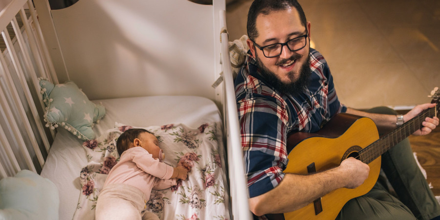 Bienfaits de la musique sur bébé : un papa jouant de la guitare pour en faire profiter à sa petite fille.