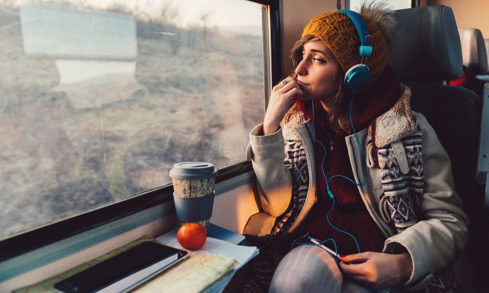 Une jeune femme dans le train ecoutant des contenus audio avec un casque pour se divertir