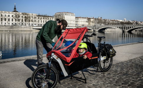 Un père asseyant ses enfants dans un de ces gros vélos, devenus tendance avec la multiplication des pistes cyclables.