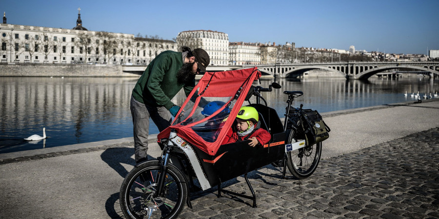 Un père asseyant ses enfants dans un de ces gros vélos, devenus tendance avec la multiplication des pistes cyclables.