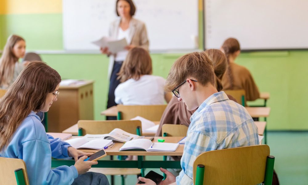 Deux jeunes collegiens en train de jouer sur leur smartphone en cours