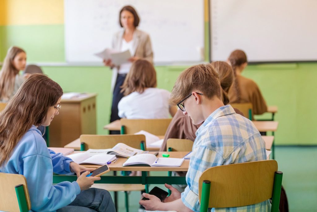 Deux jeunes collegiens en train de jouer sur leur smartphone en cours