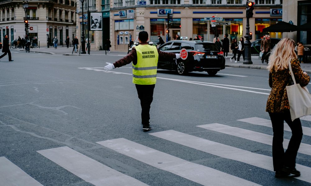 Un agent bloquant la circulation pour laisser des écoliers traverser, assurant une accessibilité de l’école pour tous.