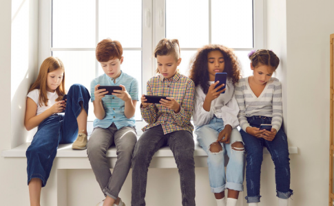 Groupe d'enfants de 11/12 ans assis sur le rebord d’une fenêtre, utilisant leur smartphone.