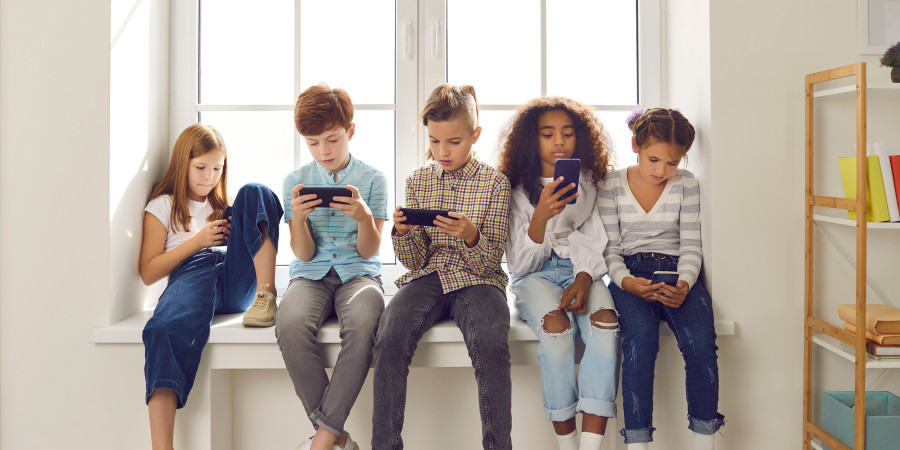 Groupe d'enfants de 11/12 ans assis sur le rebord d’une fenêtre, utilisant leur smartphone.