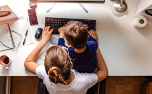 Une mère, à la maison, en train de travailler devant son PC avec son fils assis sur ses genoux.