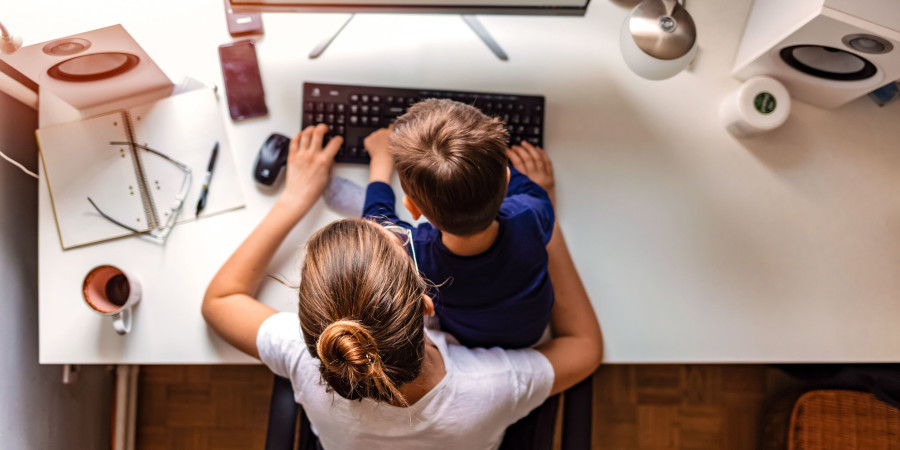 Une mère, à la maison, en train de travailler devant son PC avec son fils assis sur ses genoux.