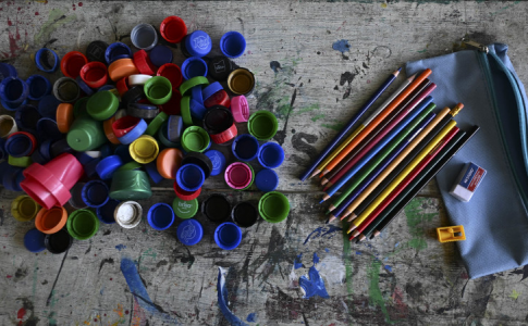 Un tas de bouchons de bouteilles à gauche et des fournitures scolaires à droite.