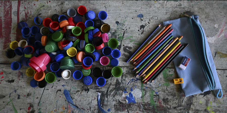 Un tas de bouchons de bouteilles à gauche et des fournitures scolaires à droite.