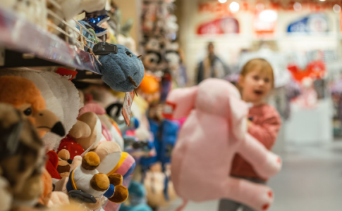 Une fillette tenant une peluche rose, devant le rayon jouet d’un supermarché.