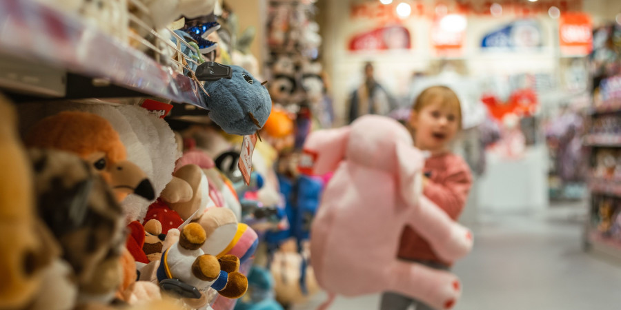 Une fillette tenant une peluche rose, devant le rayon jouet d’un supermarché.