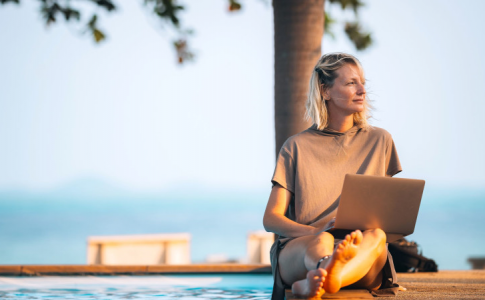 Une jeune femme assise sur une table, travaillant sur son PC, non loin de la plage.