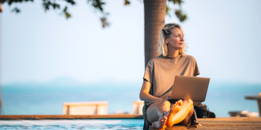 Une jeune femme assise sur une table, travaillant sur son PC, non loin de la plage.