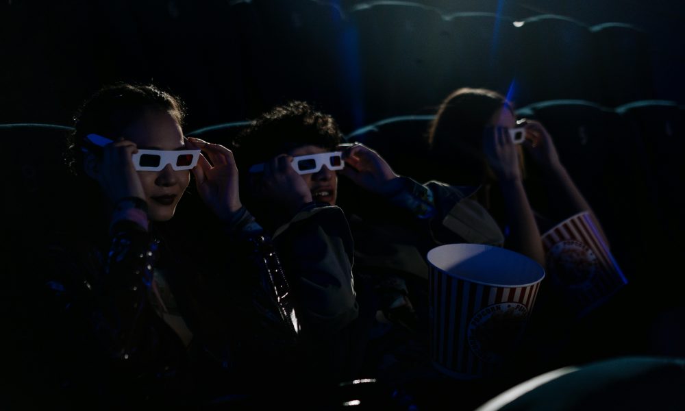 Trois jeunes en train de regarder un film au cinéma.