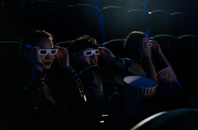 Trois jeunes en train de regarder un film au cinéma.