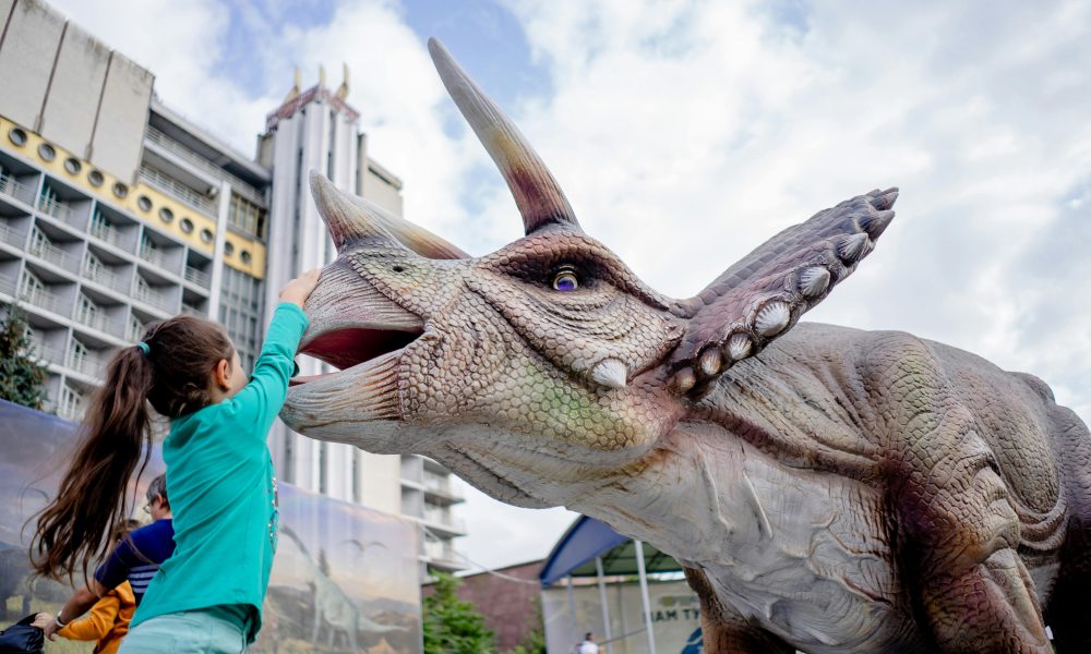 Une fillette en train de toucher une sculpture de dinosaure dans un des meilleurs musées pour enfants en France.