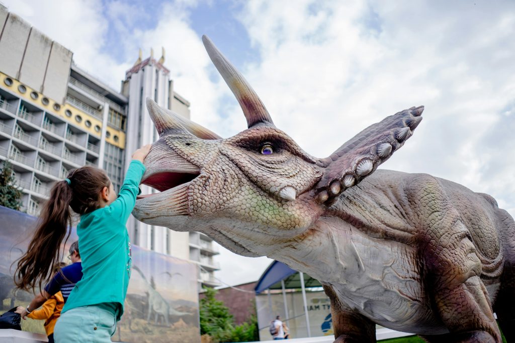 Une fillette en train de toucher une sculpture de dinosaure dans un des meilleurs musées pour enfants en France.