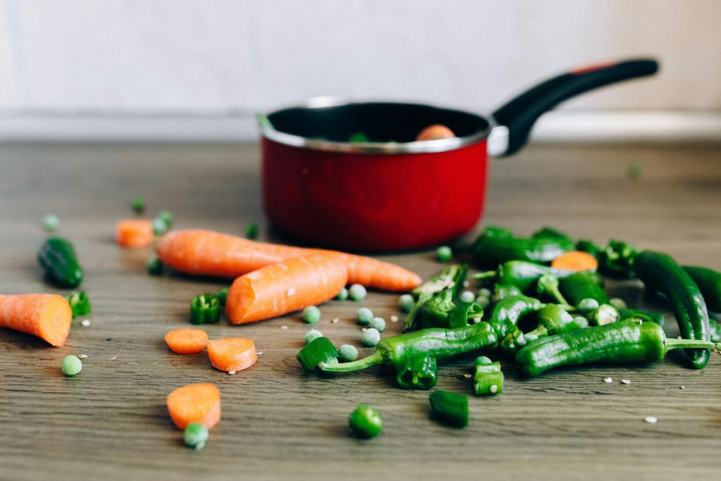 De restes de légumes frais découpés à côté d’une casserole contenant des aliments à cuire.