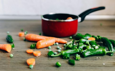 De restes de légumes frais découpés à côté d’une casserole contenant des aliments à cuire.